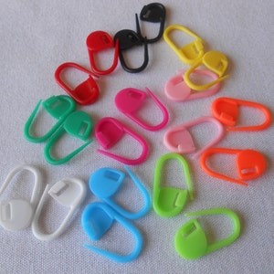 May include: A set of 15 colorful plastic stitch markers in various colors, including red, yellow, green, blue, pink, orange, and white. The markers are shaped like a small oval with a hook on one end.