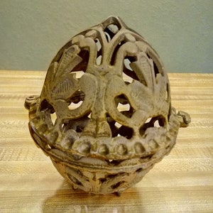 May include: A decorative, ornate, metal, cage-like sphere with a floral design. The sphere is made of a light brown metal and has a delicate, intricate design.