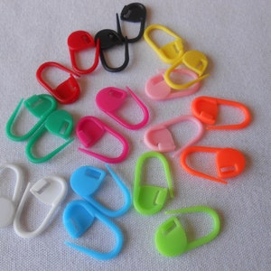 May include: Assortment of colorful plastic stitch markers in various shapes and sizes. The markers are used to keep track of rows or stitches in knitting or crocheting projects.