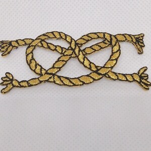 May include: A gold rope knot embroidered patch with black thread outlining the rope. The knot is a double figure eight knot.