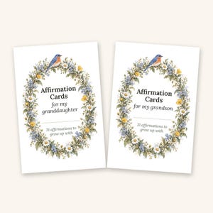 May include: Two white rectangular affirmation card sets featuring a floral wreath illustration with a blue bird. One set reads Affirmation Cards for my granddaughter, the other reads Affirmation Cards for my grandson, both with 31 affirmations to grow up with.