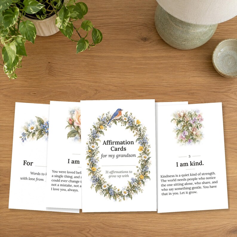 May include: A set of white affirmation cards for a grandson, featuring watercolor floral wreaths and a blue bird. The central card reads Affirmation Cards for my grandson, 31 affirmations to grow up with. Other cards display text and floral art.