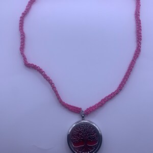 Puede incluir: Un collar trenzado rosa y gris con un colgante de plata con un diseño de árbol de la vida.