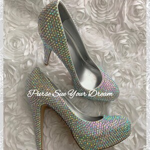 May include: A pair of high-heeled pumps completely covered in iridescent, light-reflecting crystals. The shoes feature a platform sole and a thin stiletto heel. The text "Purse Sue Your Dream" is overlaid in white script across the center of the image.