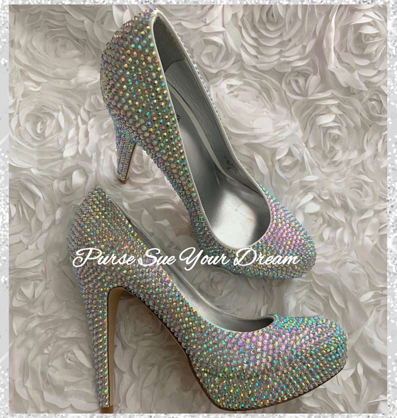 May include: A pair of high-heeled pumps completely covered in iridescent, light-reflecting crystals. The shoes feature a platform sole and a thin stiletto heel. The text "Purse Sue Your Dream" is overlaid in white script across the center of the image.
