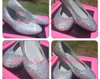 Op de afbeelding: Een paar zilveren ballerina's volledig bedekt met heldere, reflecterende strass-steentjes. De schoenen hebben een ronde neus en een gladde, lichtgekleurde binnenvoering. De tekst "Purse Sue Your Dream" is over de vier panelen heen geplaatst.