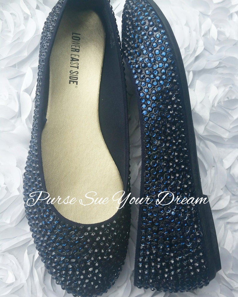 May include: A pair of flat shoes covered in dark blue rhinestones. The interior insole is gold and features the text LOWER EAST SIDE. The text Purse Sue Your Dream is overlaid on the image. The shoes have a rounded toe and a low profile design.
