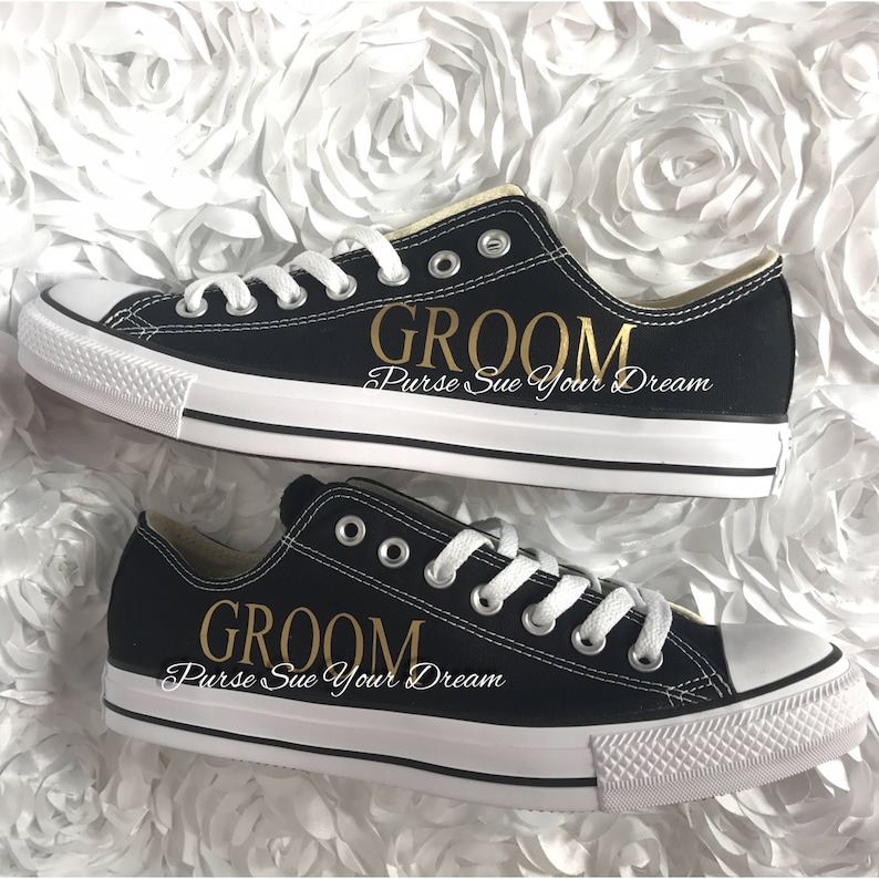 May include: A pair of black low-top sneakers with white laces and white rubber toe caps. The side of each shoe features the word GROOM in gold lettering, with the text Purse Sue Your Dream printed in white script underneath the gold text.