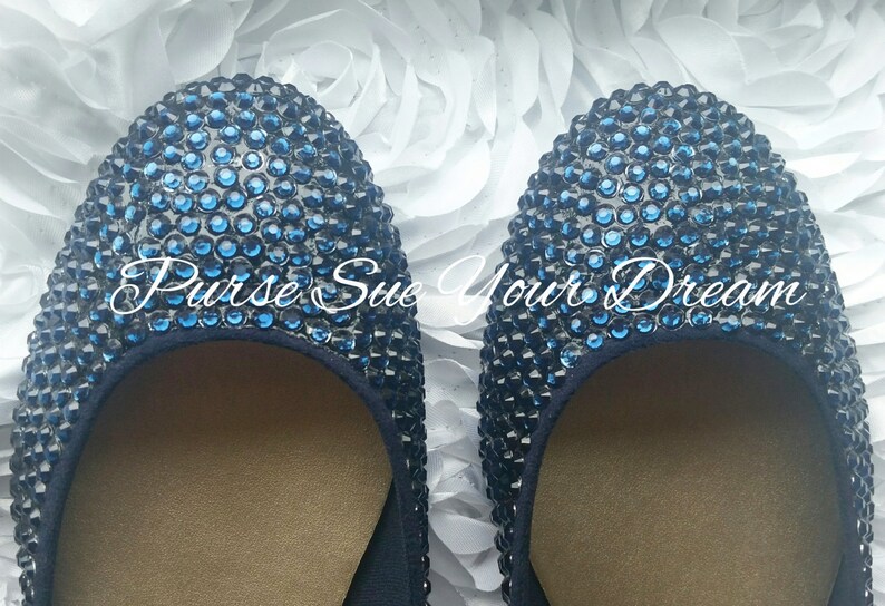 May include: A pair of round-toe flats completely covered in small, dark blue rhinestones. The interior of the shoes features a tan lining. The text "Purse Sue Your Dream" is overlaid in white script across the center of the two shoes.