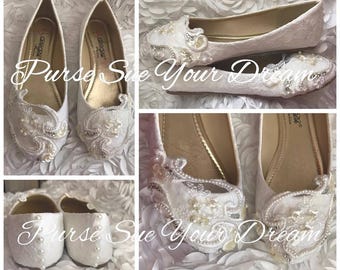 May include: A pair of white flat shoes featuring lace fabric, embellished with white pearls and clear beads in a swirling pattern on the toe. The interior is gold, and the heel features a vertical row of small white pearls. Text reads Purse Sue Your Dream.