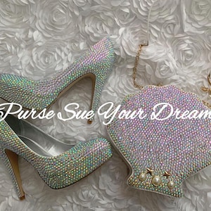 May include: A pair of high-heeled pumps and a shell-shaped clutch bag, both fully encrusted with iridescent crystals. The clutch features a gold chain strap and three pearl and star accents. The text "Purse Sue Your Dream" is overlaid on the image.
