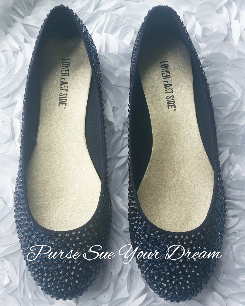 May include: A pair of black ballet flats covered in small, dark, reflective rhinestones. The interior insoles are gold-toned and feature the text "LOWER EAST SIDE" printed in black. The text "Purse Sue Your Dream" is visible at the bottom.