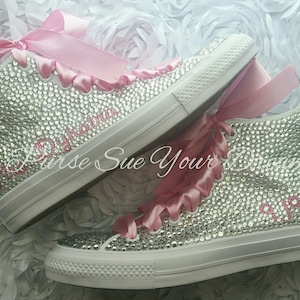 May include: A pair of high-top sneakers completely covered in clear rhinestones, featuring pink satin ribbon laces. The text Mrs. Dykatra is embroidered in pink on the side of one shoe, and the date 9.19.15 is embroidered on the other.