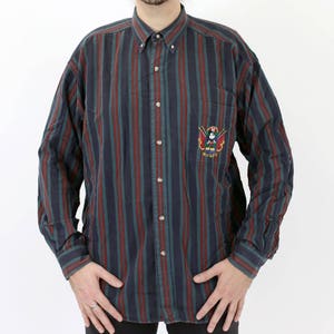 May include: A striped long-sleeved button-down shirt with a red, blue, and green color scheme. The shirt has a small embroidered logo on the left chest that says "Mickey".