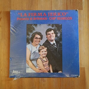 Op de afbeelding: Een blauwe vinyl platenhoes met de tekst "LA FIRMA JERICÓ" en "Presenta al distinguido CHIP REARDON". De hoes toont een foto van een gezin met een man, een vrouw en een jonge jongen.