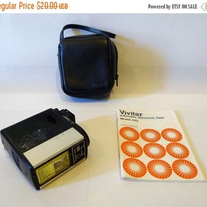 以下が含まれることがあります： 黒いビビター自動電子フラッシュユニット、モデル252、黒い革ケースと取扱説明書付き。取扱説明書は、オレンジ色の円と「ビビター自動電子フラッシュモデル252取扱説明書」というテキストが書かれた白い表紙です。