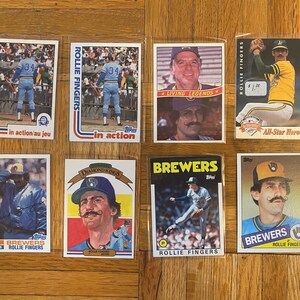 May include: A collection of nine baseball trading cards featuring images of baseball player Rollie Fingers. The cards are from different years and feature different photos of Fingers in various poses. The cards are all in good condition and would be a great addition to any baseball card collection.