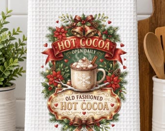 Op de afbeelding: Een witte theedoek met wafelstructuur voorzien van een centrale afbeelding van een mok warme chocolademelk met marshmallows, omringd door een feestelijke krans van dennentakken, rode kerststerren, gouden bellen en linten.