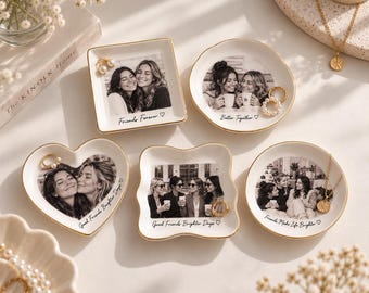 May include: Five white ceramic trinket dishes with gold-painted rims, each featuring a black and white photograph of friends and custom text. Shapes include a square, circle, heart, and wavy-edged square, displaying jewelry like rings and necklaces.