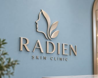 May include: A three-dimensional wall sign featuring the text RADIEN SKIN CLINIC in a metallic finish. Above the text is a stylized icon of a human profile silhouette combined with three leaf shapes, all mounted on a light blue wall.