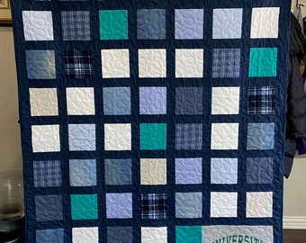 May include: A blue and white quilt with a variety of fabrics, including plaid, denim, and solid colors. The quilt is made up of 36 squares, and the bottom right square features a University of North Dakota logo.
