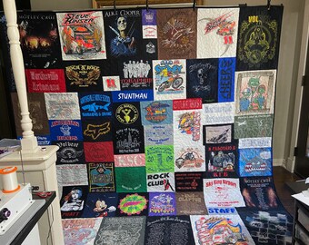 May include: A quilt made from a variety of t-shirts, featuring band logos, sports teams, and other designs. The quilt is made up of squares of different colours and patterns, and is a unique and personal piece of art.