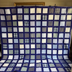 May include: A large rectangular quilt featuring a grid of alternating solid navy blue squares and various light blue, white, and plaid patterned fabric squares. The quilt is constructed with a consistent navy blue sashing between each square.