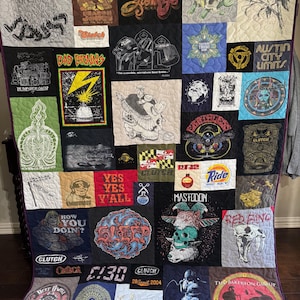 Pode incluir: Uma colcha de retalhos feita com várias camisetas de bandas de música. A colcha apresenta uma variedade de bandas, incluindo Bad Brains, Clutch, Mastodon, Red Fang e The Bakerton Group. A colcha é feita de uma variedade de tecidos, incluindo algodão, sarja e flanela. A colcha é uma ótima maneira de mostrar seu amor pela música e suas bandas favoritas.