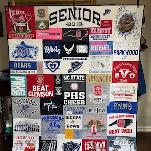 Peut inclure: Une courtepointe en patchwork multicolore composée de divers t-shirts graphiques. La courtepointe présente le texte SENIOR 2018 en haut, entouré de nombreux logos, noms d'écoles et imprimés liés au sport, notamment NC State, Parkwood et le cheerleading.