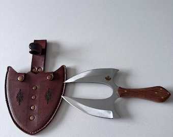 Peut inclure: Un couteau de lancer à double lame avec un manche en bois et un petit emblème de feuille d'érable sur la lame, accompagné d'un étui en cuir marron foncé avec des coutures décoratives, des rivets métalliques et une boucle de ceinture.