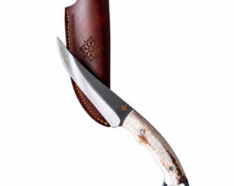 Könnte beinhalten: Ein feststehendes Messer mit einer geschwungenen silbernen Stahlklinge, einem strukturierten Knochengriff und einem Metallring am Knauf. Ein kleines Ahornblatt-Symbol ist auf die Klinge geätzt. Es wird mit einer dunkelbraunen Lederscheide geliefert.