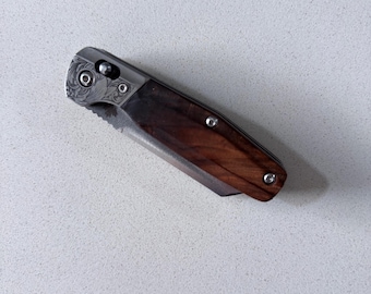Peut inclure: Un couteau de poche pliant doté d'un manche en bois brun foncé avec un motif de grain visible. La mitre est en métal argenté avec une gravure florale complexe. Le couteau est fixé par trois petites vis de couleur argentée.