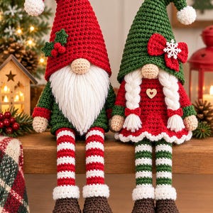 May include: Two crochet gnome dolls with long dangling legs. The left gnome wears a red hat with holly, a green shirt, and red-and-white striped legs. The right gnome has white braided hair, a green hat with a red bow, and green-and-white striped legs.