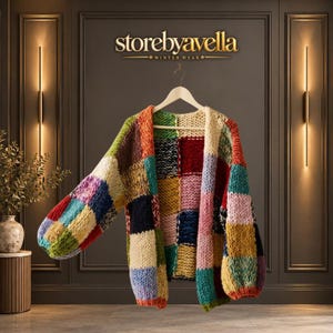 Puede incluir: Un cárdigan de punto grueso con un diseño de retazos multicolor con cuadrados grandes en tonos rojo, azul, amarillo, verde y crema. La prenda tiene mangas largas, frente abierto y se muestra en una percha de madera con el texto storebyavella.