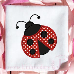 May include: A white square fabric with a red ladybug design. The ladybug has white polka dots on its wings and black accents. The text "Joyous Embroidery" is printed in the bottom right corner.