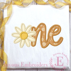 May include: A white onesie with a brown and white embroidered "one" with a white daisy on the left side. The text "Joyous Embroidery" is at the bottom of the onesie.