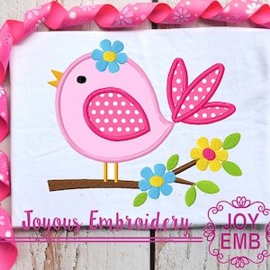 May include: A pink bird with white polka dots and a blue flower on its head is perched on a brown branch with flowers. The bird is on a white background with the text "Joyous Embroidery".