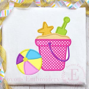 Puede incluir: Un diseño con temática de playa con un cubo rosa con lunares, una estrella de mar amarilla y una pala verde. También se incluye un balón de playa con secciones azules, amarillas, rosas y moradas. El diseño está sobre un fondo blanco.