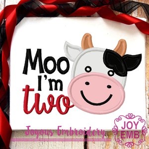 May include: Embroidered design on a white fabric with the text "Moo I'm Two" in red and black lettering. A cartoon cow face with a black patch on its head is to the right of the text.