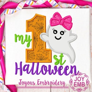 Pode incluir: Tecido branco com um design temático de Halloween. Apresenta o texto "my 1st Halloween" em verde e roxo, um número 1 laranja com teias de aranha e um fantasma sorridente com um laço rosa. A frase "Joyous Embroidery" também está presente.