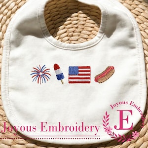 Pode incluir: Um babador branco para bebê com desenhos bordados de um fogo de artifício vermelho, branco e azul, um picolé, uma bandeira americana e um cachorro-quente. O texto Joyous Embroidery está impresso em rosa no canto inferior direito.