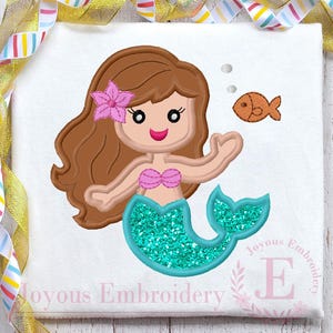 Può includere: Un design a cartoni animati di una sirena con capelli castani, un fiore rosa e una coda glitterata turchese. La sirena indossa un top a conchiglia rosa e si protende verso un pesce arancione. Il design è su sfondo bianco.