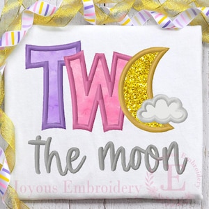 May include: Embroidered design on a white fabric with the text "TWO the moon" in gray. The number "TWO" is in pink and purple with a watercolor effect. A gold glitter crescent moon with a white cloud is next to the word "TWO".