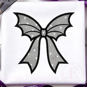 May include: A white fabric square featuring a black embroidered bow with bat-wing shaped loops and tails. The bow has a mesh-like texture with small white star accents throughout. The text Joyous Embroidery is visible in the bottom corner.