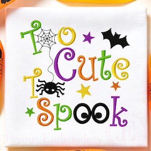 May include: A white fabric square featuring machine embroidery with the text "Too Cute to Spook" in colorful, curly lettering. The design includes a black spider hanging from a web, a black bat, and several small stars in purple, yellow, and orange.