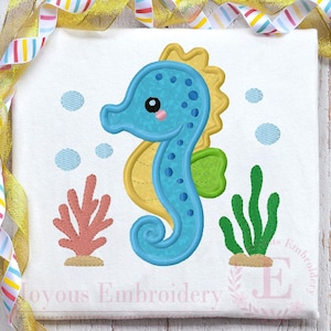 May include: A white fabric square featuring a blue seahorse design with yellow and green accents. Coral and seaweed are also depicted, along with blue bubbles. The text "Joyous Embroidery" is at the bottom.