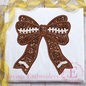 May include: A brown glitter bow with white stitching, resembling a football. The bow is outlined in a darker brown and is centered on a white background. The text "Joyous Embroidery" is at the bottom.