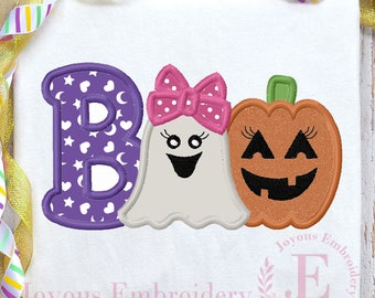 May include: White t-shirt featuring a Halloween design. The word "BOO" is spelled out with a purple letter B, a ghost with a pink bow, and an orange jack-o'-lantern. The letter B is decorated with white stars and moons.