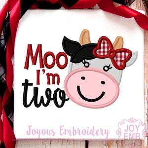 May include: White t-shirt with a cow face design and the text "Moo I'm two". The cow has a pink nose, a red and white checkered bow, and black and tan accents. The words "Joyous Embroidery" are at the bottom.