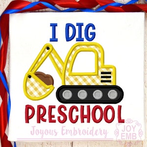 Può includere: T-shirt bianca con un design di escavatore a scacchi gialli e bianchi. Il testo "I DIG PRESCHOOL" è ricamato in blu e rosso. Il design include una benna marrone e cingoli neri.